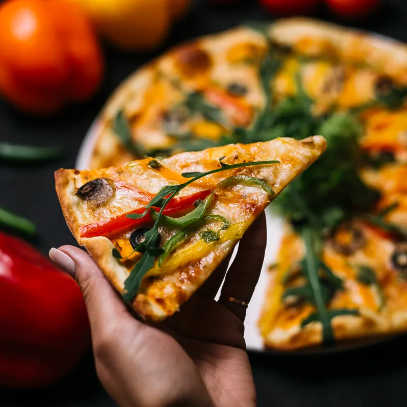 side-view-hand-holding-slice-italian-pizza-with-colorful-bell-peppers-mushrooms-black-olives-urugula-cheese-scaled-300x300