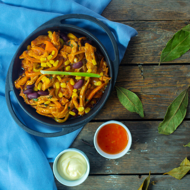 top view of chicken stew with vegetables and corns in a pan served with sweet chili sauce on rustic background