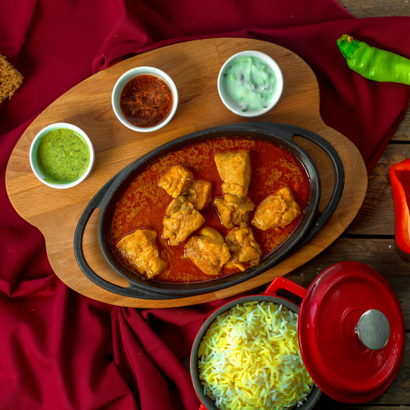 top view of chiken stew with garlic in tomato sauce served with spices on a wooden board