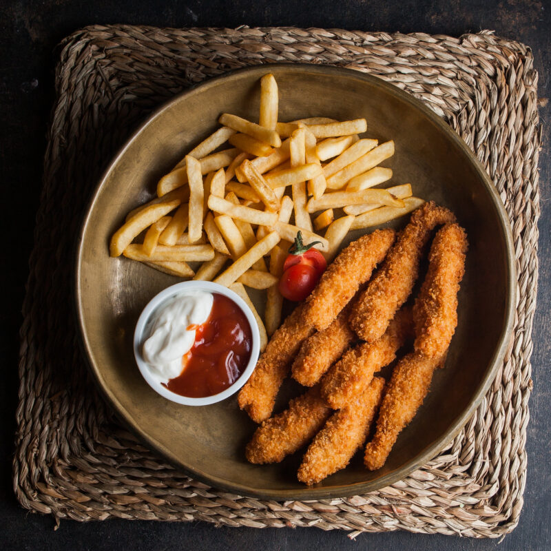 Top view chicken nuggets with french fries and tomato and sous in clay dishes on stone background