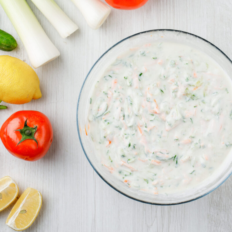 Yogurt salad in a bowl with vegetables and lemons flat lay on a white wooden background