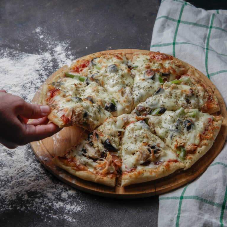 Side view pizza on a wooden stand with a tablecloth on a dark background, hand take a slice of pizza
