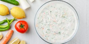 Yogurt salad in a bowl with vegetables and lemons flat lay on a white wooden background